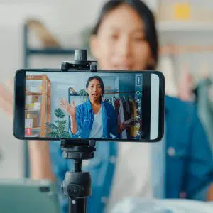A content creator recording a video with a smartphone mounted on a tripod, enthusiastically addressing her audience with welcoming gestures about TikTok Marketing ideas.
