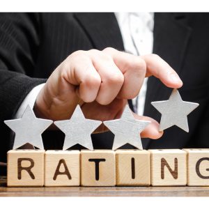 A businessperson is positioning a fifth star above wooden blocks that spell out "rating," symbolizing the act of enhancing a hotel's reputation through a top review.